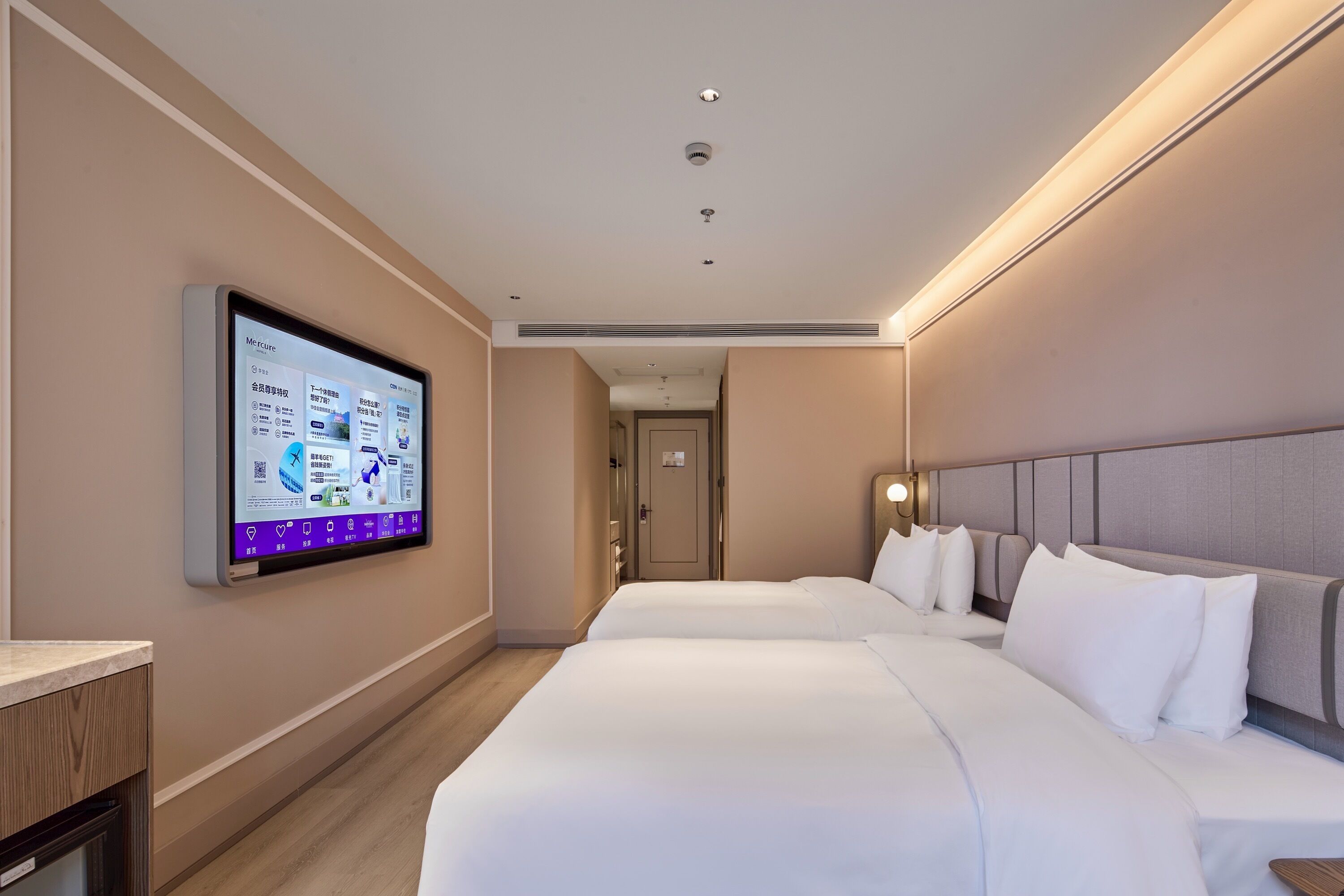 A hotel room with two beds, a flat-screen TV mounted on the wall, and a wooden desk.