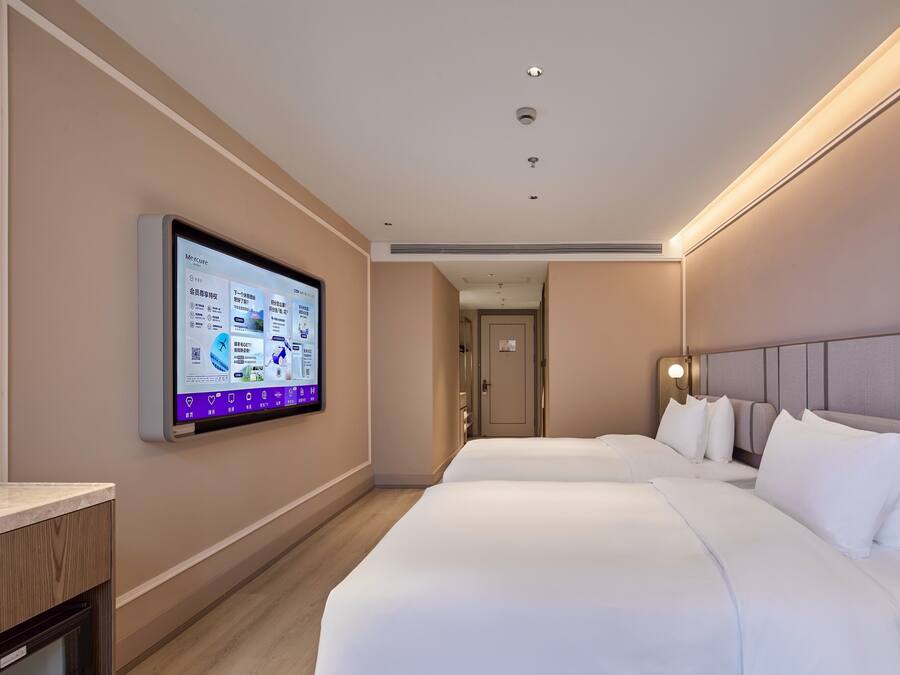 A hotel room with two beds, a flat-screen TV mounted on the wall, and a wooden desk.
