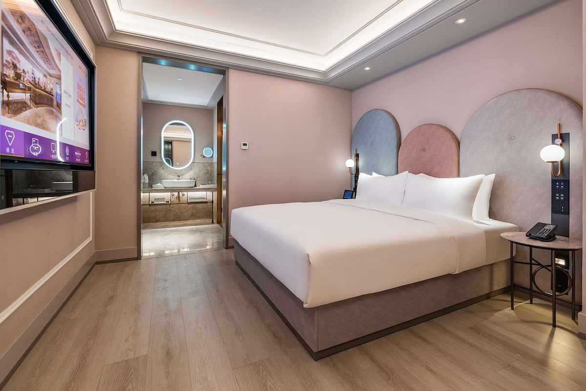 A modern hotel room with a large bed, bedside table, and a TV mounted on the wall.