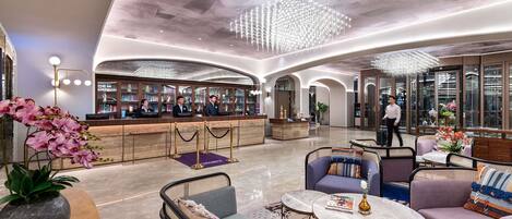 A spacious lobby with a reception desk, seating areas, and a large chandelier.