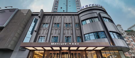 A modern hotel with a prominent 'Mercure' sign, featuring a curved facade and large windows.