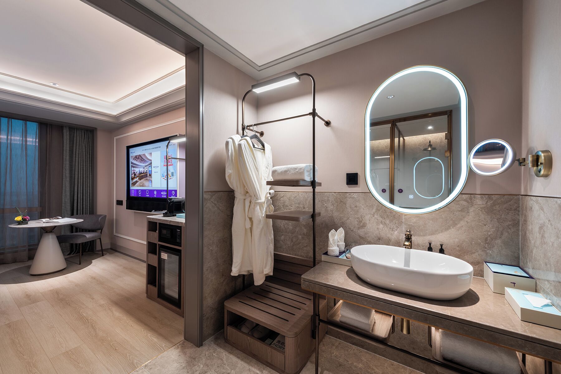 A modern bathroom with a large mirror, a sink, and a shower. There is a TV in the adjacent room.