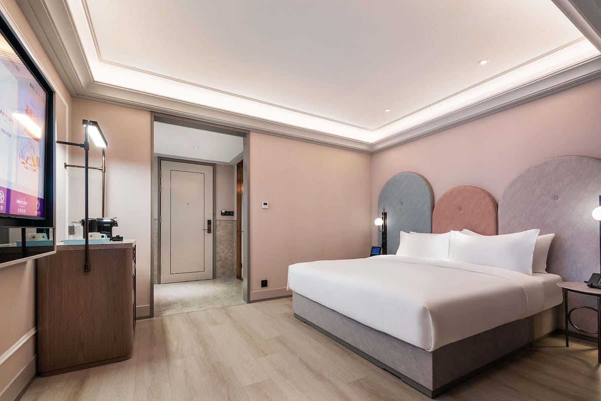 A modern hotel room with a large bed, a desk, and a television.