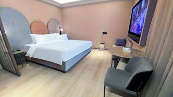 A modern hotel room with a bed, a desk, a chair, a TV, and a trash bin.