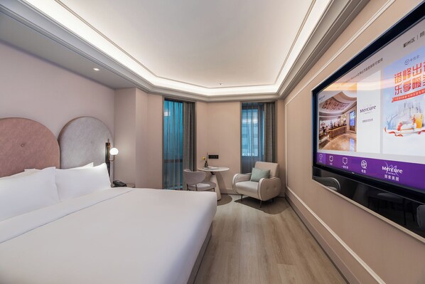A hotel room with a large bed, a desk, two chairs, a TV screen displaying hotel information, and a view of the outside through the window. - Mercure Ningbo Yinzhou (Ningbo)