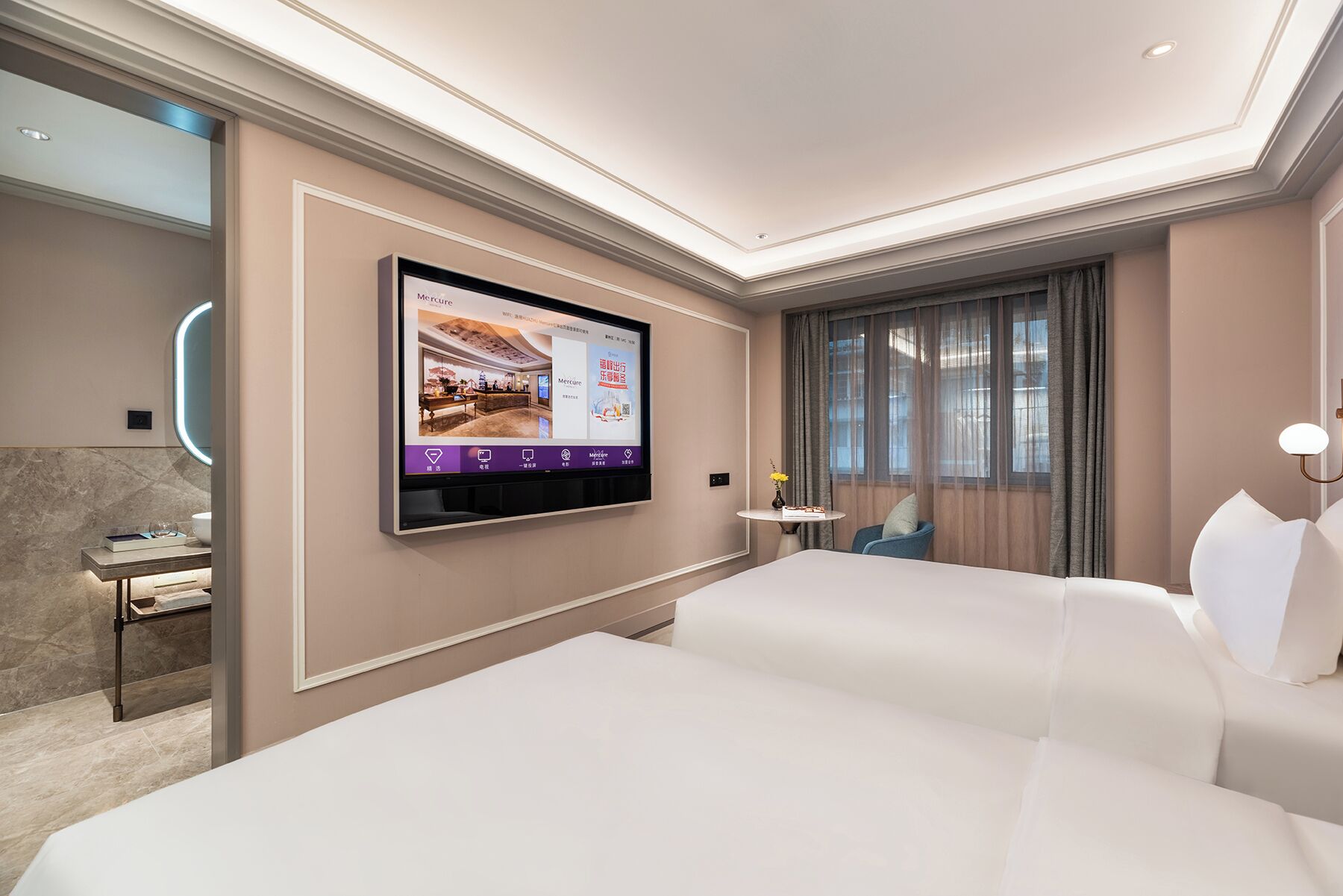A hotel room with a large bed, a TV mounted on the wall, a small table with a vase, and a window with curtains.