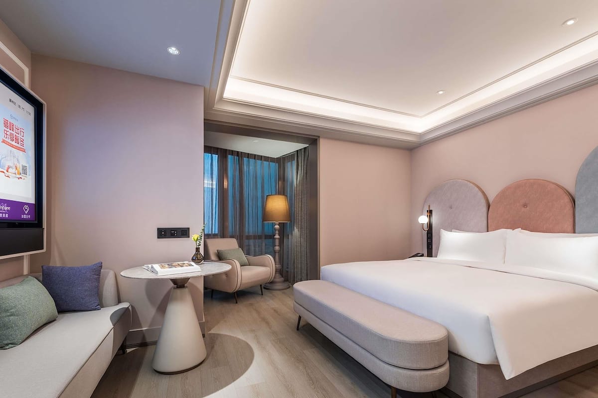 A modern hotel room with a large bed, a sofa, a small table, and a TV.