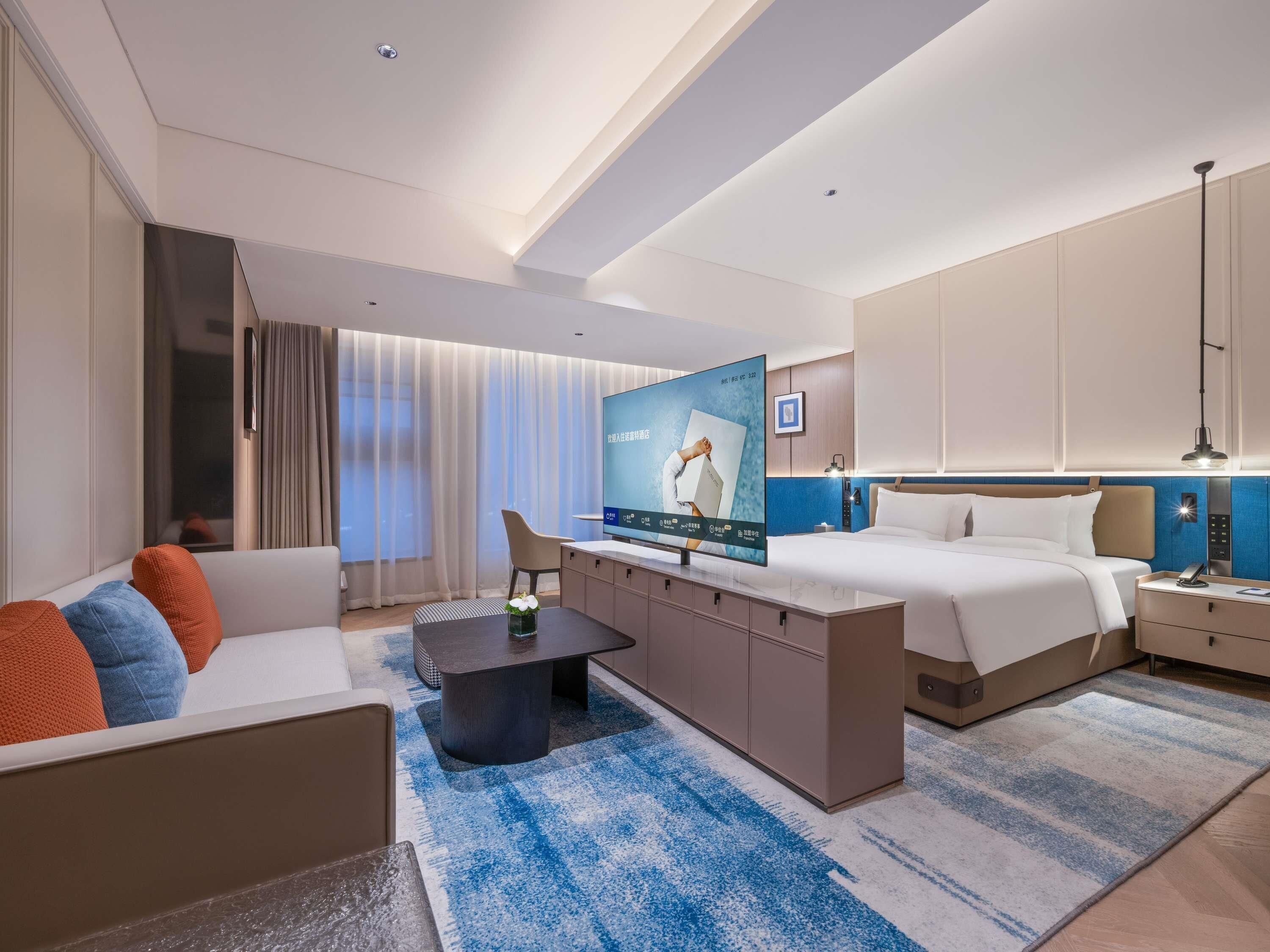 Une chambre d’hôtel moderne équipée d’un lit, d’un canapé, d’une télévision, d’un bureau et d’une table de chevet.