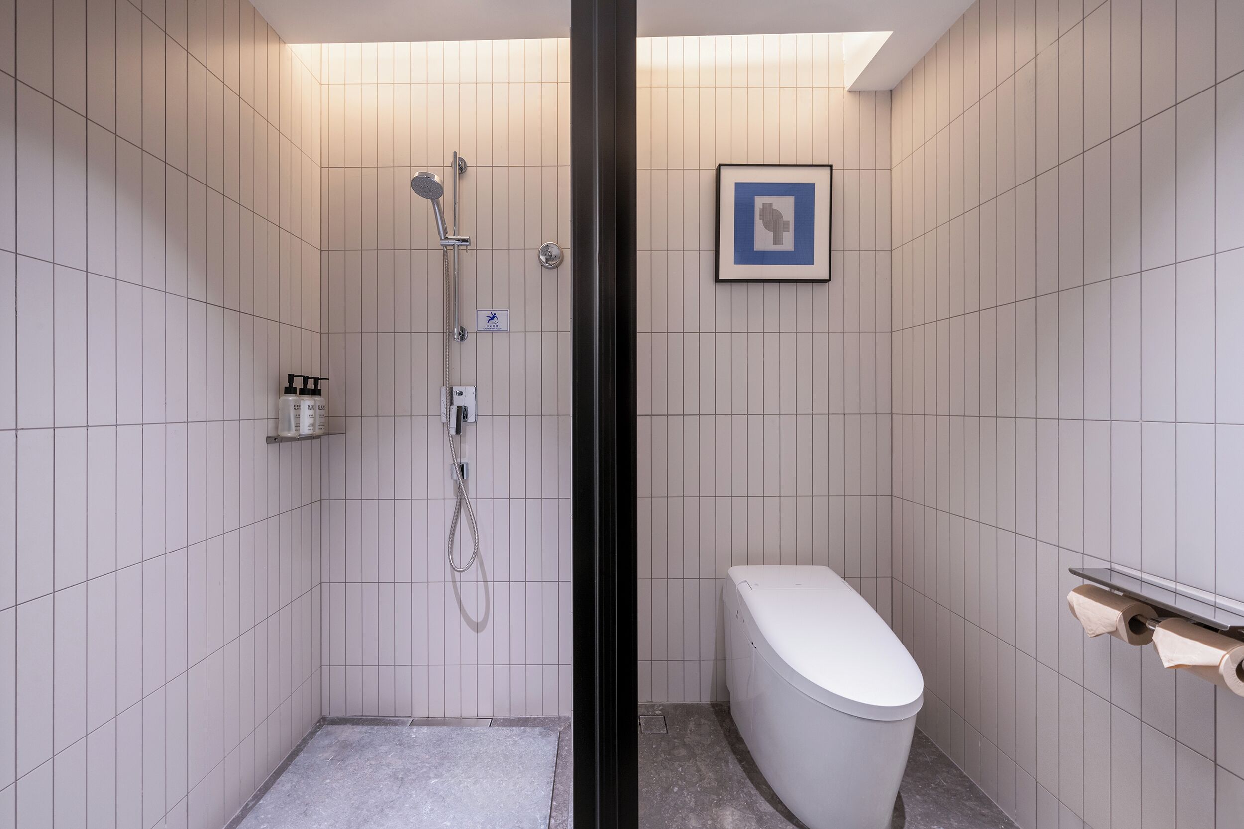 A modern bathroom with a shower, toilet, and a framed picture on the wall.