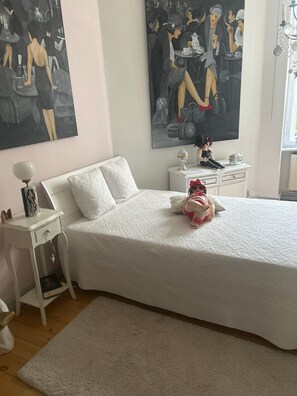A bedroom with a large bed, a nightstand, a dresser, and two paintings on the wall.