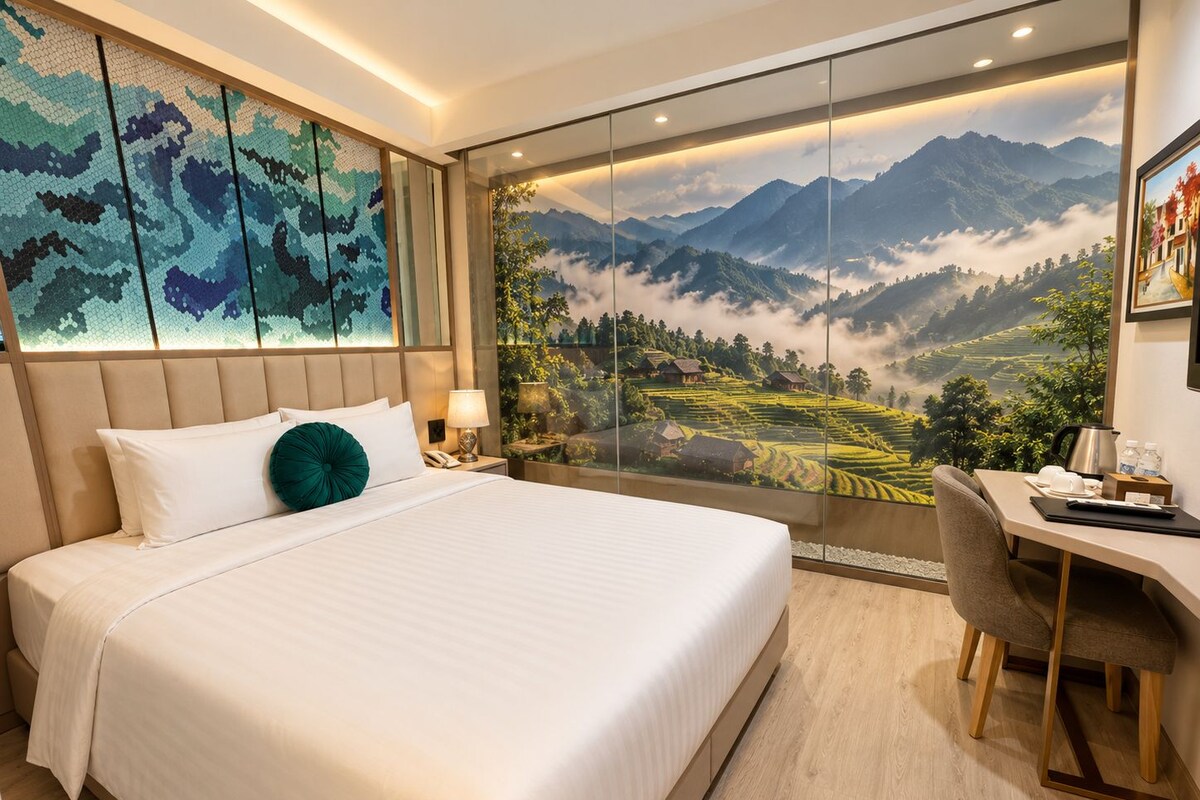 A hotel room with a large bed, a desk, and a scenic mountain view through a glass wall.
