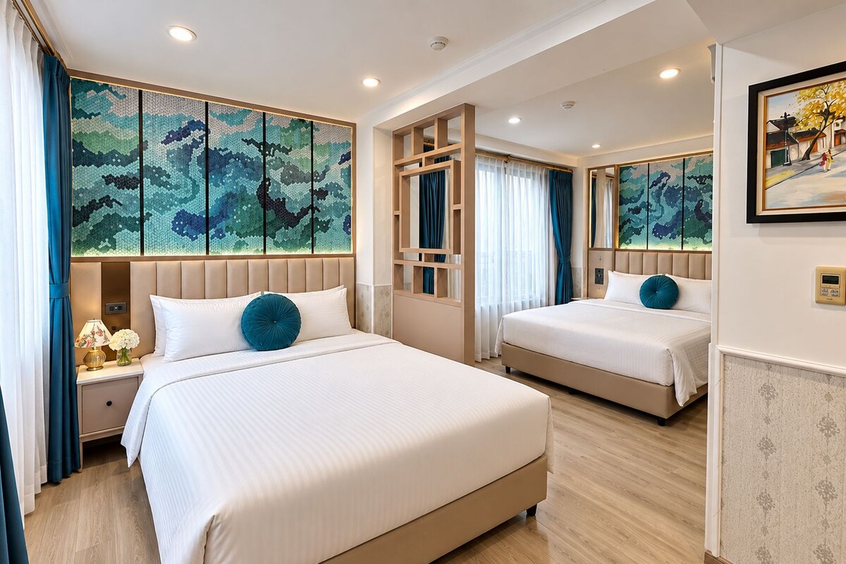 A hotel room with two beds, a large window, a decorative wall, and a painting.