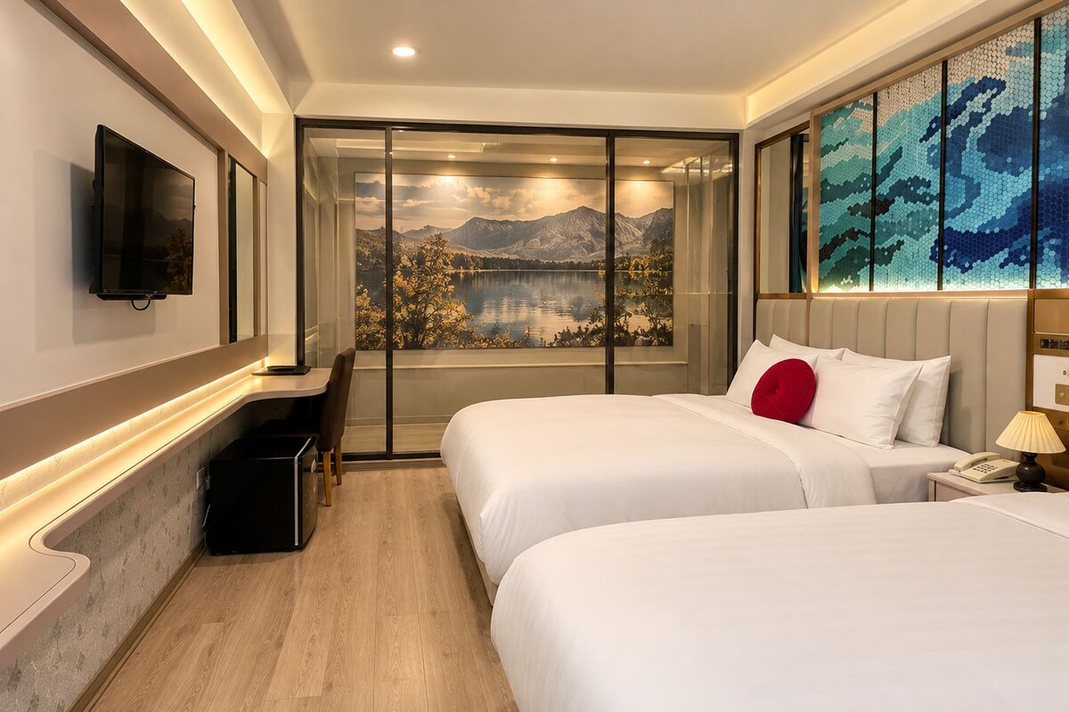 A hotel room with two beds, a desk, a TV, and a large window with a mountain view.