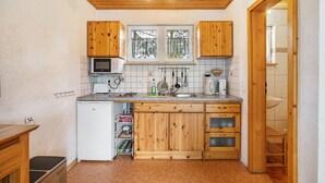 Une cuisine compacte avec des meubles en bois, un four à micro-ondes, un évier et une fenêtre donnant sur les arbres.