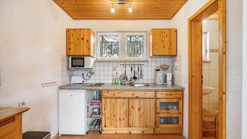 Eine kompakte Küche mit Holzausstattung, einer Mikrowelle, einem Spülbecken und einem Fenster mit Blick auf Bäume.
