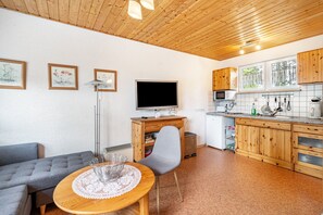 Une cuisine moderne avec des meubles en bois, un coin repas comprenant une table et des chaises, et un téléviseur à écran plat fixé au-dessus du comptoir.