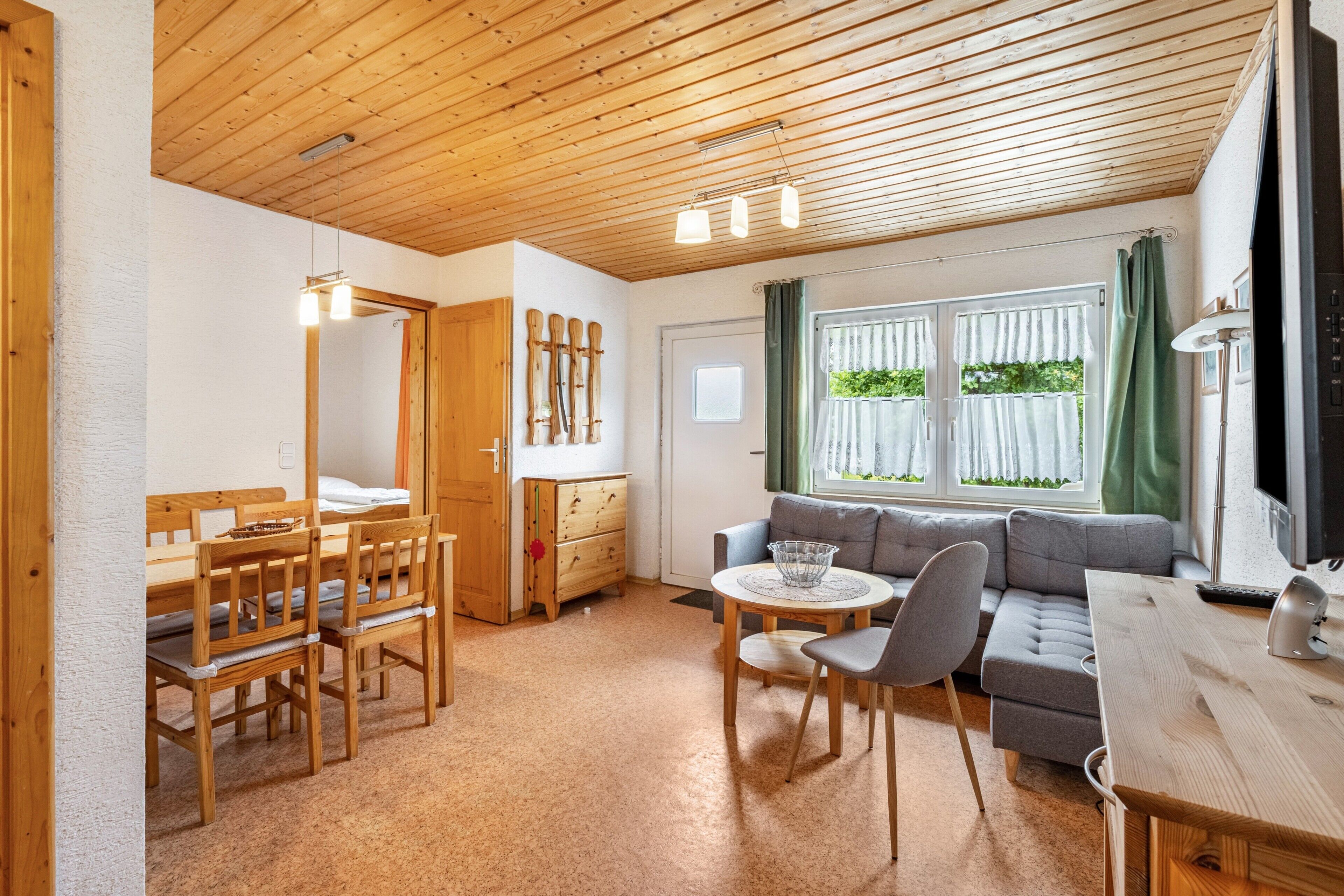 A wooden ceiling, a dining table with chairs, a sofa, and a television.
