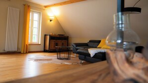 A living room with a wooden floor, a black sofa, a glass vase, and a wooden cabinet.