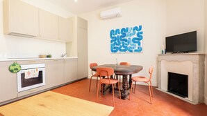 A modern kitchen with white cabinets, a dining table with orange chairs, a fireplace, and a flat-screen TV. - Apartment Mirage Villa Cana (Cannes)
