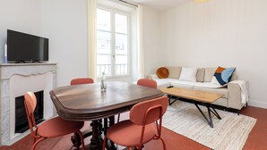 A dining area with a wooden table and chairs, a television on a mantelpiece, and a sofa with cushions. - Apartment Mirage Villa Cana (Cannes)