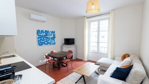 A modern living room with a dining area, a sofa set, a TV, and a large window. - Apartment Mirage Villa Cana (Cannes)