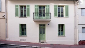 Ein Gebäude mit einer grünen Tür, mehreren Fenstern mit grünen Rollläden und einem Balkon mit einem Metallgeländer.