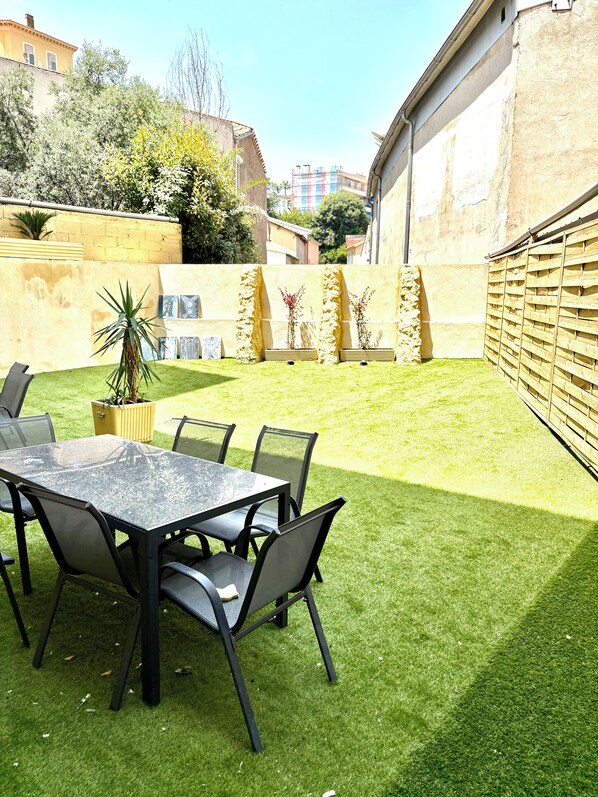 A patio with a table and chairs, surrounded by a well-maintained lawn and a stone wall. - Solea apartment, Villa cana private garden (Cannes)