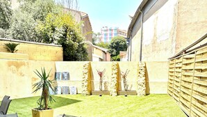 A patio with a table and chairs, surrounded by a well-maintained lawn and a stone wall. - Apartment Azzura, Villa Cana private garden (Cannes)