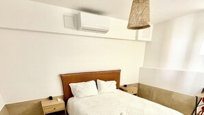 A hotel room with a large bed, a bedside table, a nightstand, a hanging light fixture, and a wall-mounted air conditioner. - Apartment Azzura, Villa Cana private garden (Cannes)