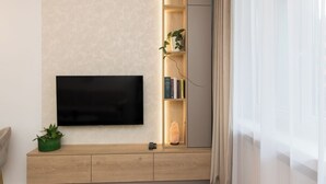 Una sala de estar moderna con un televisor de pantalla plana montado en una pared con textura, una mesa consola de madera con una planta verde y una estantería con libros y objetos decorativos.