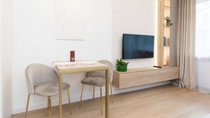 Una sala de estar moderna con un diseño minimalista, que incluye un mueble de televisión de madera, un televisor de pantalla plana y una pequeña mesa con dos sillas.