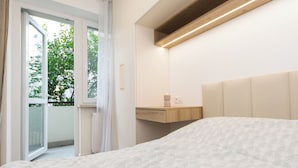 Un dormitorio con cama, mesita de noche, espejo y ventana con vista a árboles.