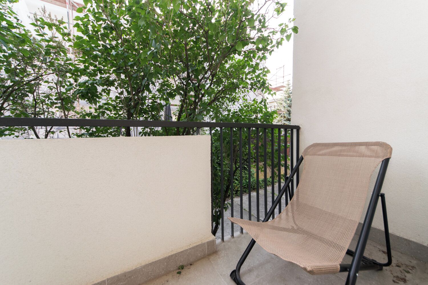 A balcony with a mesh chair, a black metal railing, and a tree in the background.