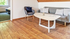 Ein modernes Wohnzimmer mit Holzboden, einem grauen Sofa mit gemusterten Kissen, einem grauen Sessel und einem weißen Marmor-Couchtisch.