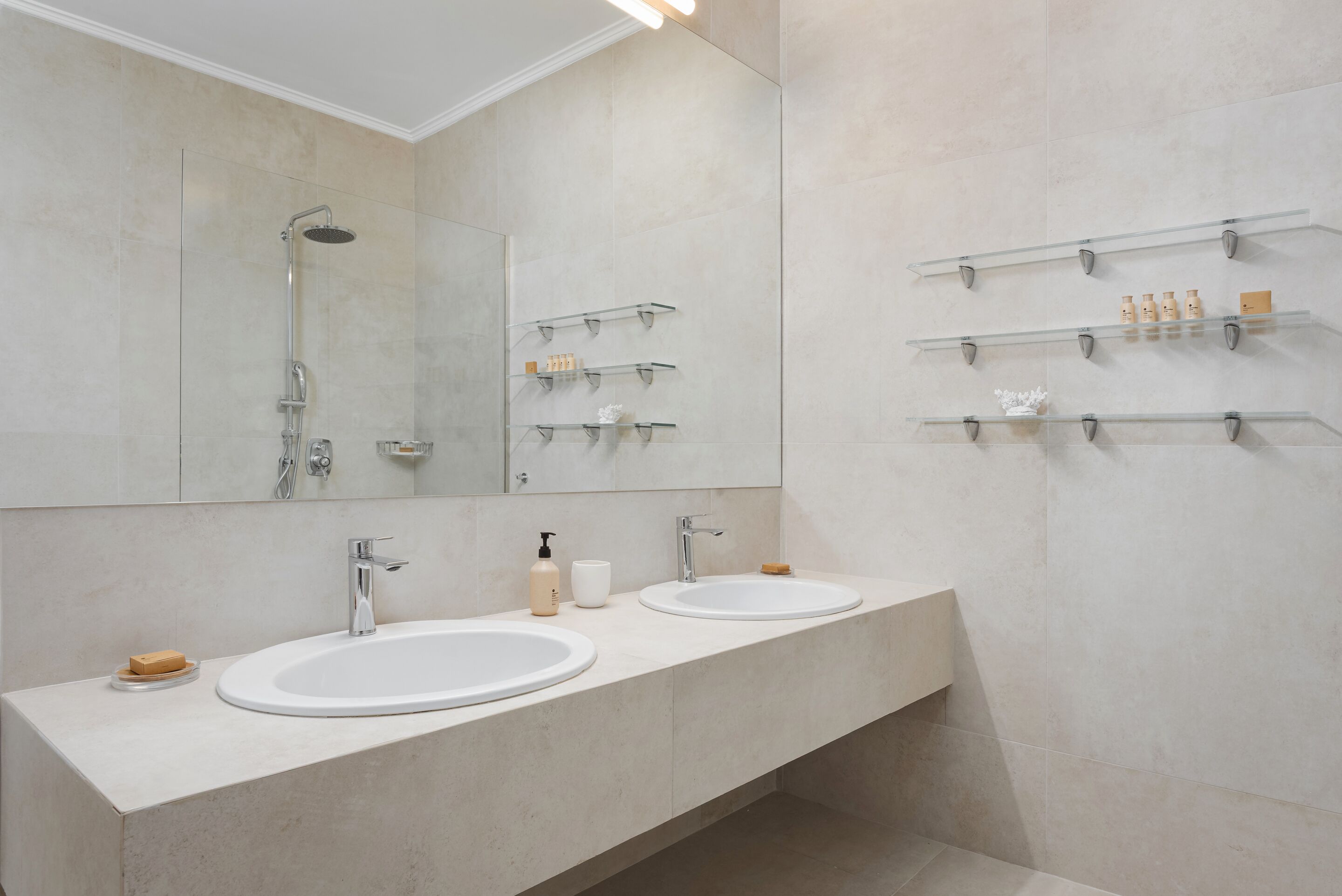A modern bathroom with two sinks, a shower, and shelves with toiletries.
