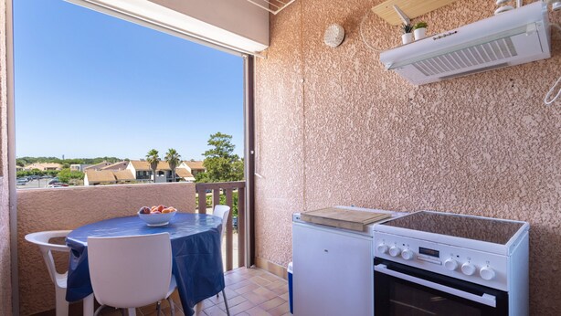 Un balcón con una mesa, sillas, un refrigerador pequeño y una estufa.
