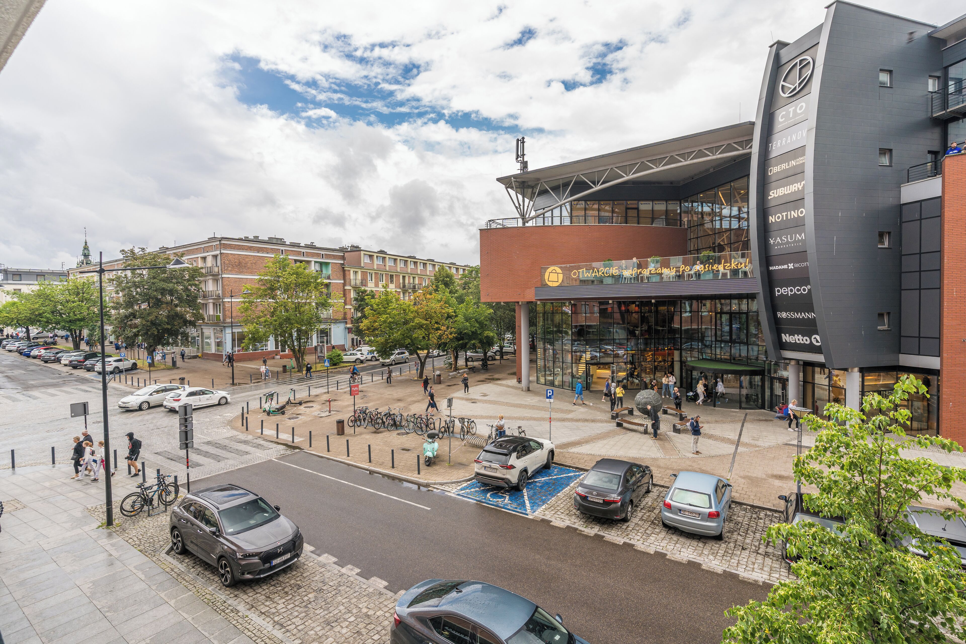 Un edificio moderno con fachada de vidrio, zona de estacionamiento y una pasarela para peatones.