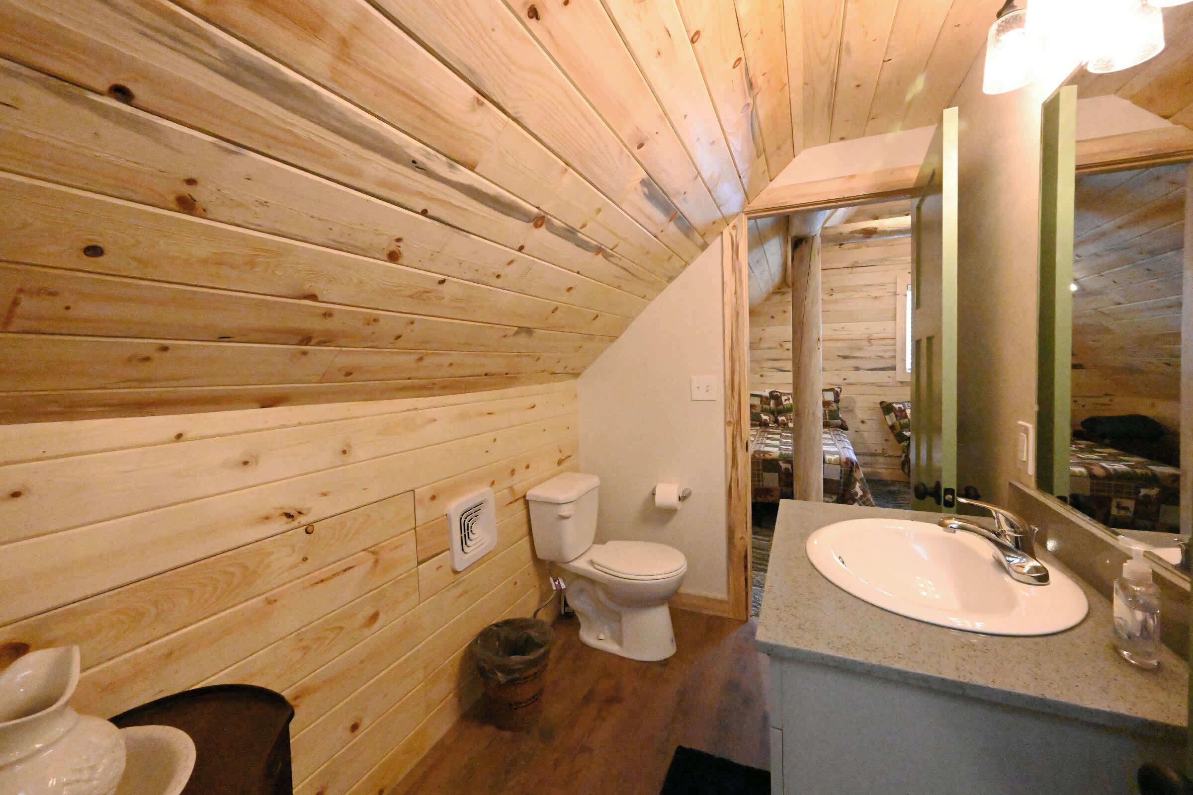 A wooden-paneled bathroom with a toilet, sink, and mirror.