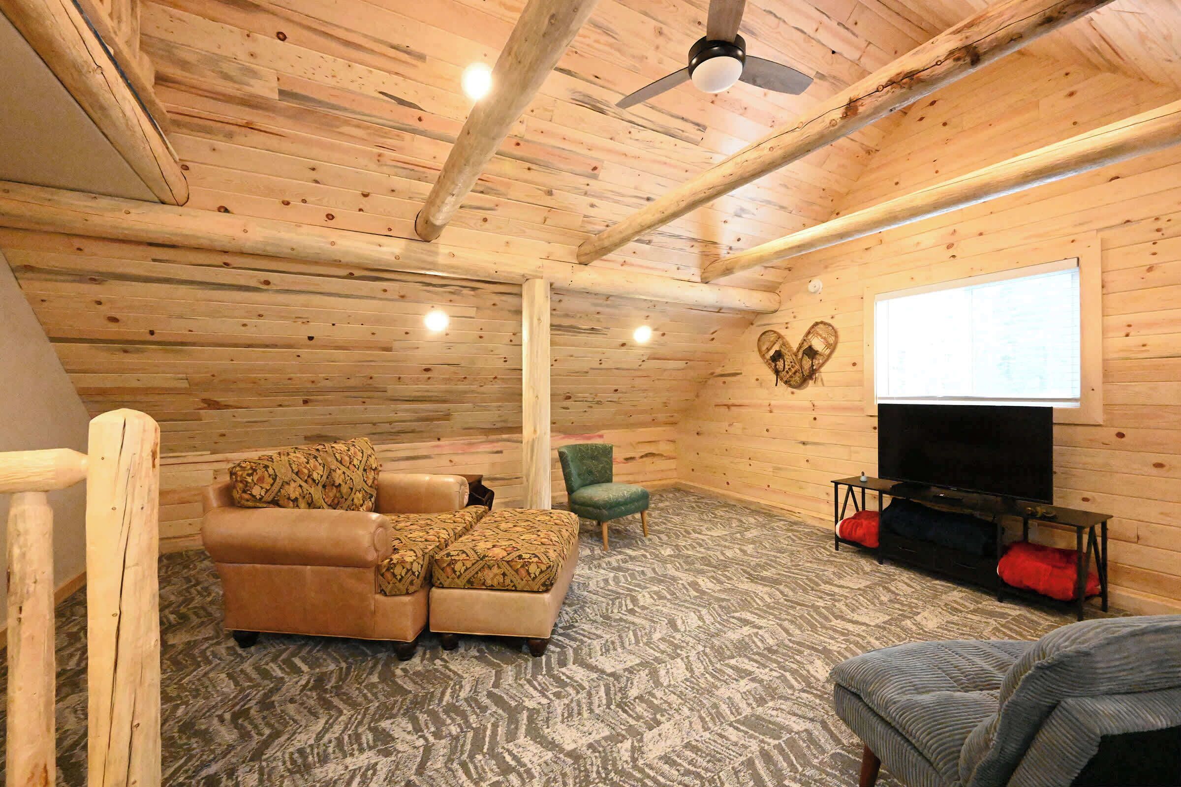 A cozy room with a wooden ceiling, a sofa, a chair, a TV, and a projector screen.