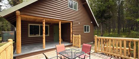 A log cabin with a wooden deck, outdoor seating, and a railing.