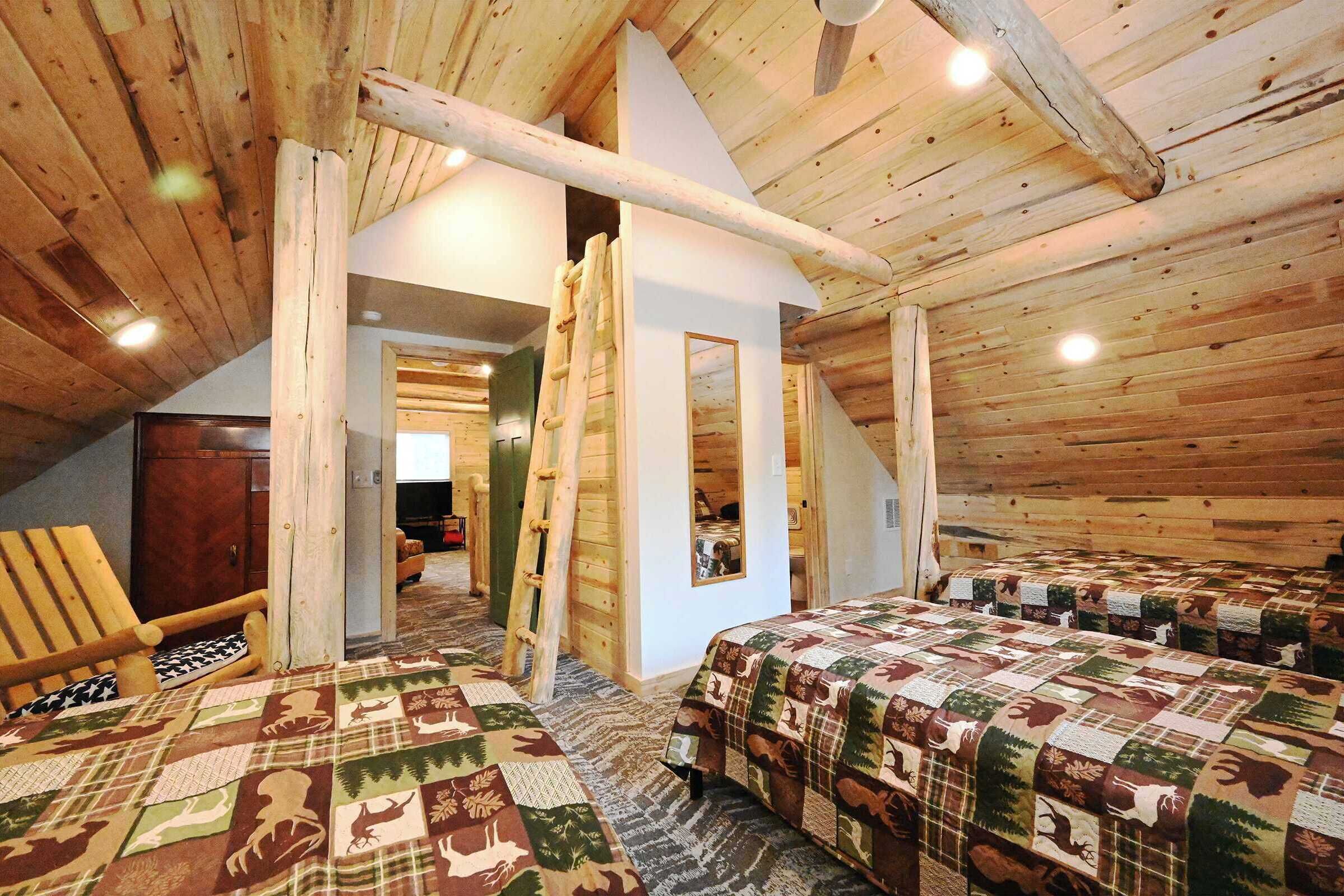 Une chambre mansardée chaleureuse avec des poutres en bois, deux lits recouverts de couvertures à motifs, une chaise en bois et une échelle.