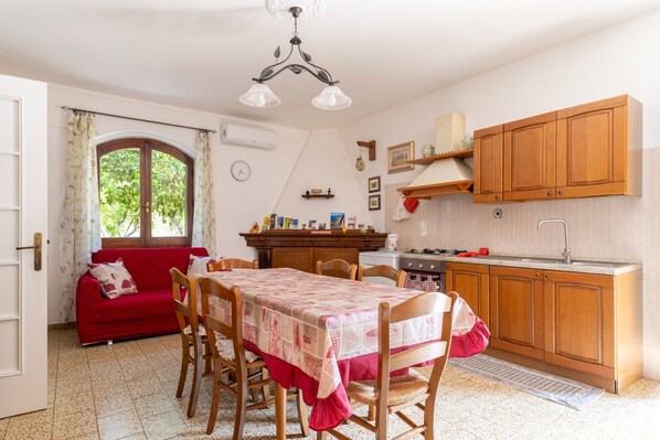 A cozy kitchen with wooden cabinets, a dining table with chairs, a red sofa, and a window with curtains.
