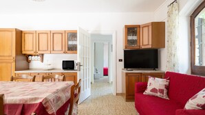 Un espacio habitable compacto con zona de comedor, kitchenette y un sofá rojo con cojines estampados.
