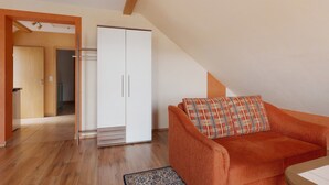 A room with a wooden floor, a white wardrobe, an orange sofa, and a patterned rug. - Apartment 'Apfelbaum' with Balcony and Wi-Fi (Obersulm)