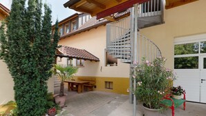 A residential building with a spiral staircase, a patio with a table and bench, and a variety of potted plants. - Apartment 'Apfelbaum' with Balcony and Wi-Fi (Obersulm)