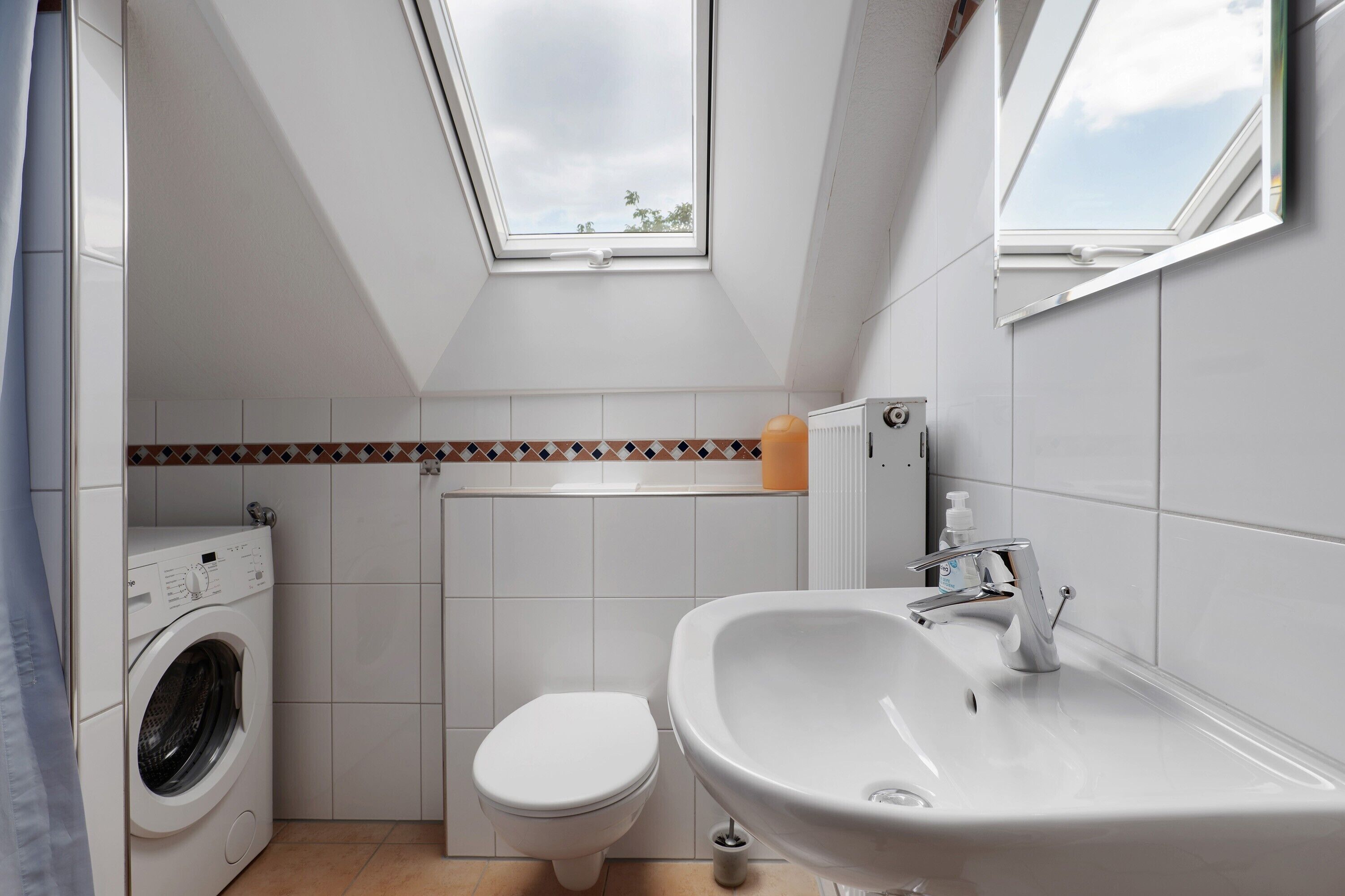 Une salle de bain compacte dotée d’un puits de lumière, d’un lave-linge, de toilettes et d’un lavabo.
