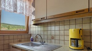 Een keuken met een raam, een spoelbak, een koffiezetapparaat en een fles handzeep.
