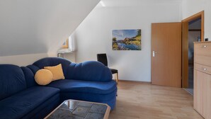 Een kamer met een blauwe bank, een houten kast en een schilderij aan de muur.