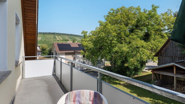 Een balkon met uitzicht op een landelijk landschap, een houten omheining en een klein houten gebouw.