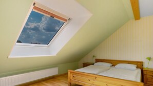 Ein Schlafzimmer mit schrägen Wänden, einem Oberlicht, einem hölzernen Bett, einem Nachttisch und einer Heizung.